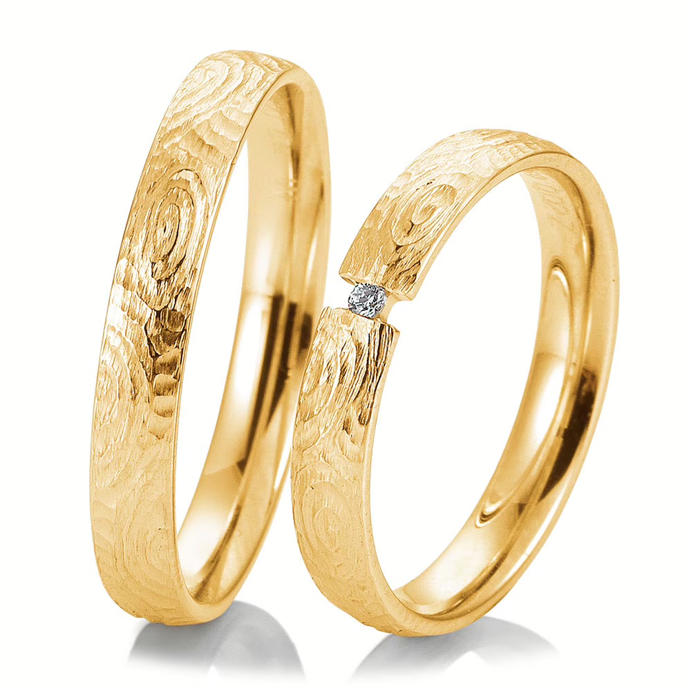 Zwei goldene Trauringe mit strukturierten Mustern; ein Ring ist mit einem kleinen, eingefassten Diamanten versehen - perfekt für moderne Bräute, die exklusive Brautmode in Aalen suchen.