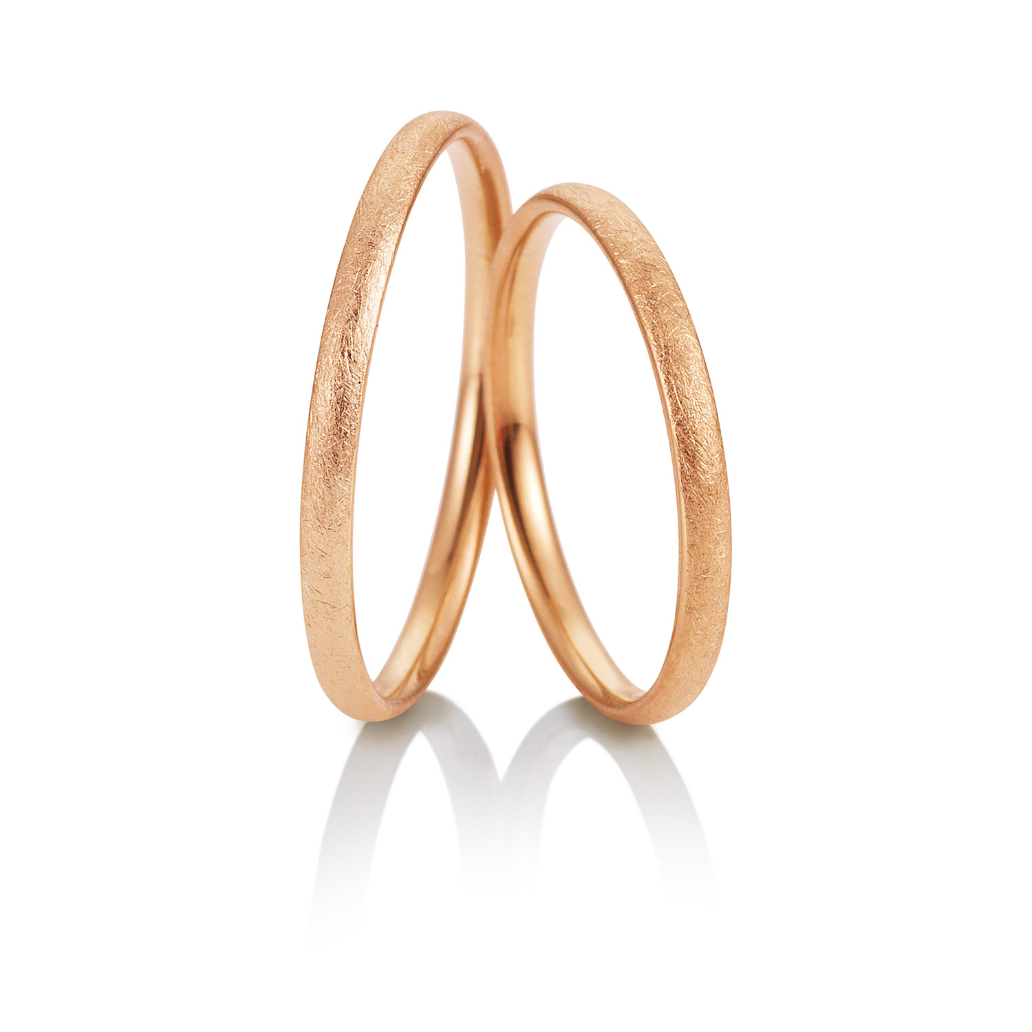 Zwei schlichte Trauringe aus Roségold stehen aufrecht auf einem weißen Hintergrund mit einer sanften Reflexion darunter, perfekt für Paare in Stuttgart, die elegante Ringe als Ergänzung zu modernen Brautkleidern suchen.