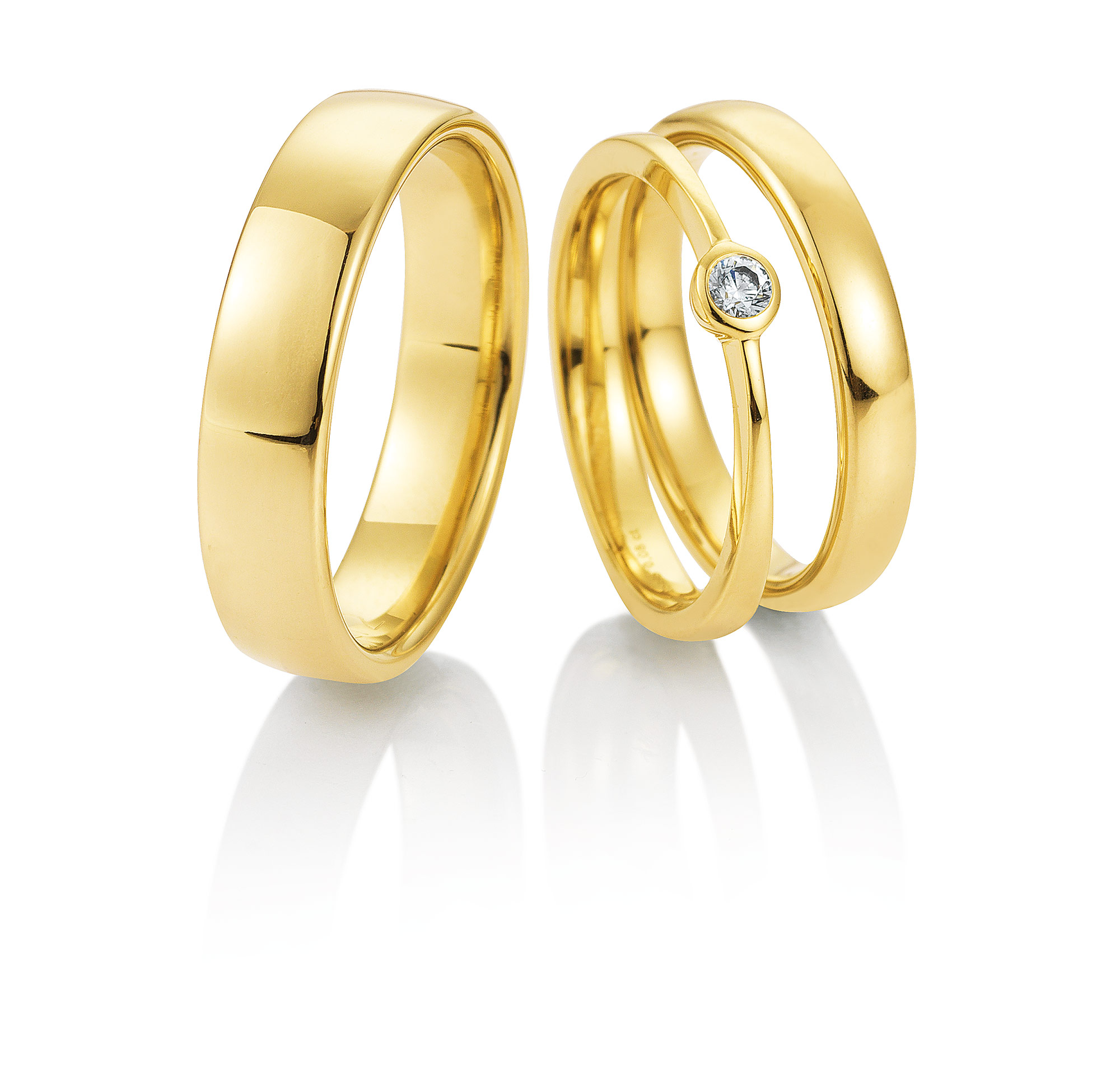 Zwei goldene Ringe - einer schlicht, einer mit einem eingefassten Diamanten - ruhen auf einer weißen, spiegelnden Oberfläche. Perfekt für moderne Bräute, die auf der Suche nach exklusiver Brautmode für ihre einzigartige Liebesgeschichte sind.